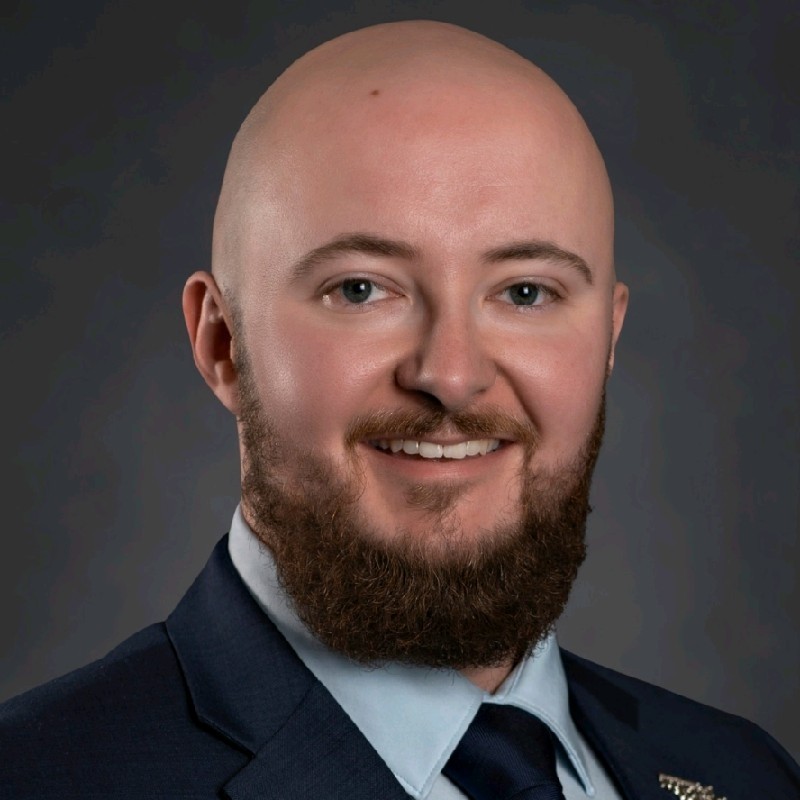 Headshot of a bald man with a beard and suit and tie