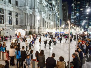 Photo of many people ice skating and watching at night with lights and next to an old beautiful building